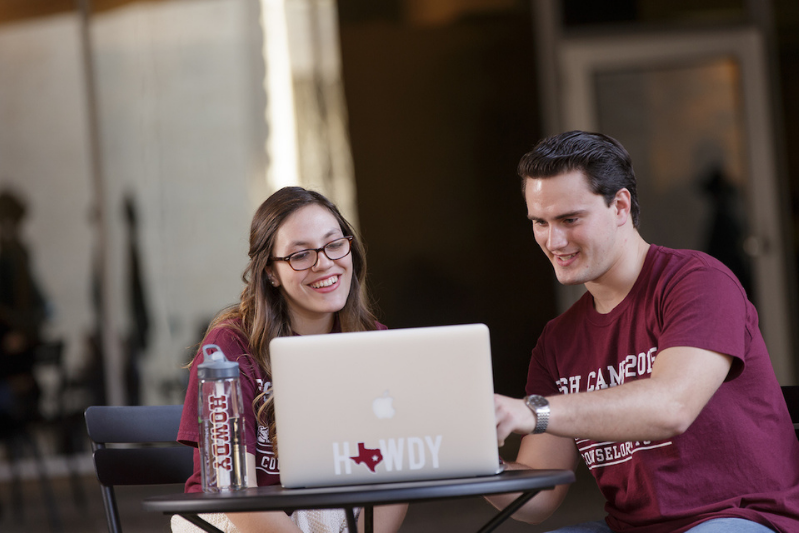 A TAMU student working on his laptop with a fellow student