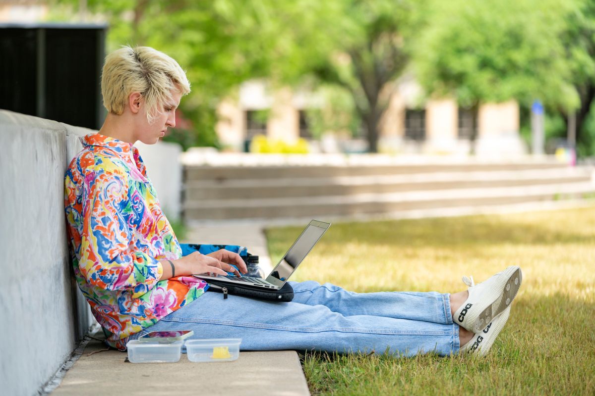 Student sitting on the grass on campus and working on their laptop